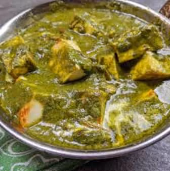 Close-up of a bowl filled with palak paneer, an Indian dish of paneer cheese cubes in a thick spinach gravy.