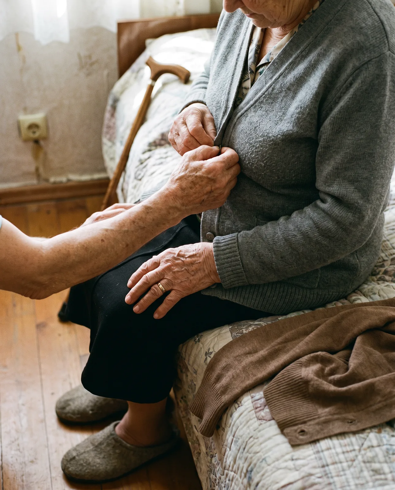Hilfe beim Ankleiden: Pflegekraft knöpft einer Seniorin die Strickjacke zu