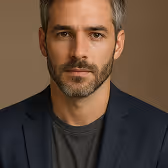 Portrait of a man with short hair, beard, and blue shirt in front of a dark blue background.