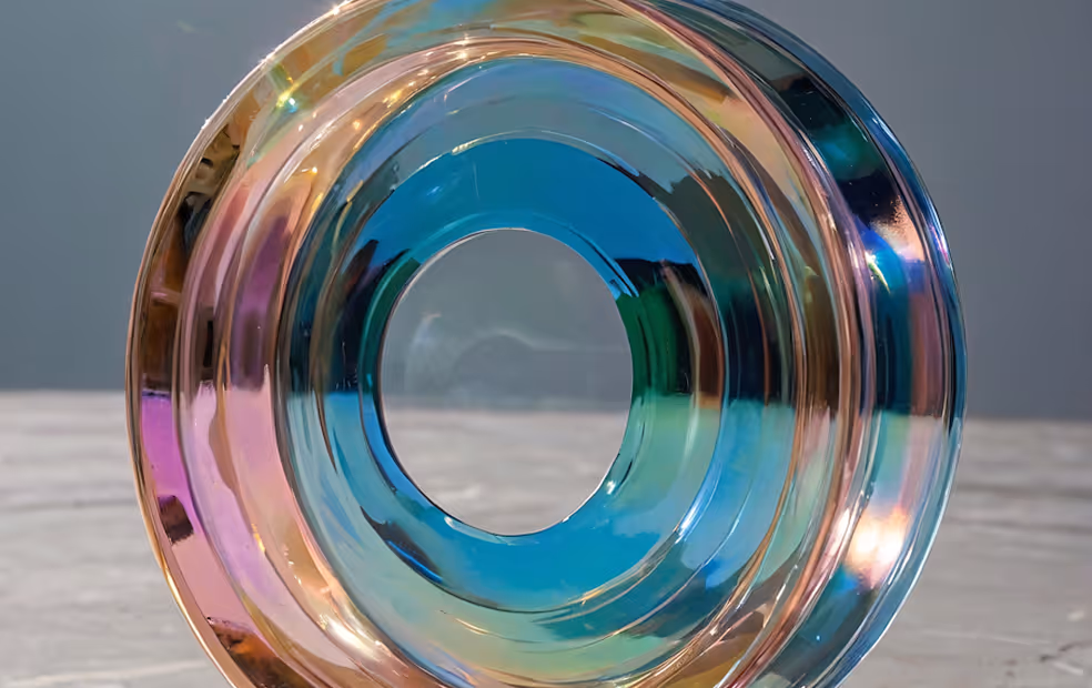 Close-up of a multicolored glass ring with a hollow center on a gray surface.