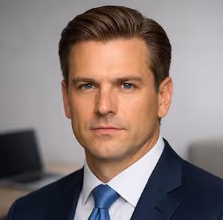 Serious man in navy suit and blue tie with neatly combed hair, facing forward against a blurred background.