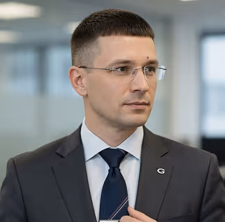 Man in dark suit with glasses and striped tie looking to the side in an office setting.