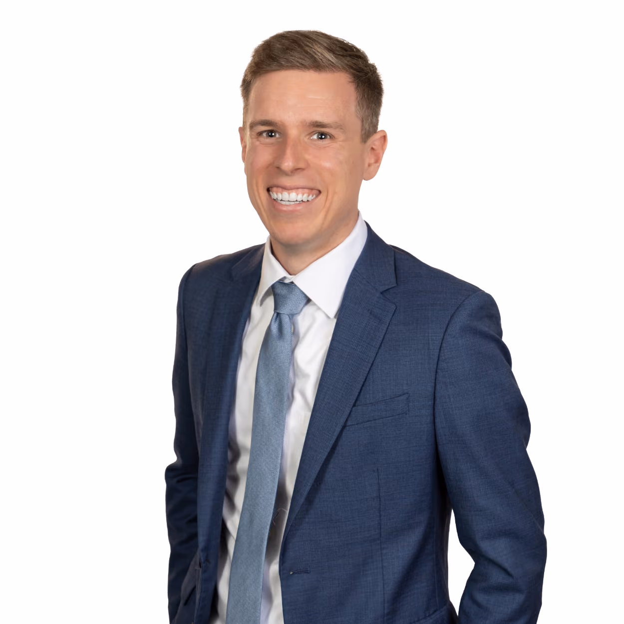 Smiling man wearing a blue suit jacket, white shirt, and light blue tie against a white background.