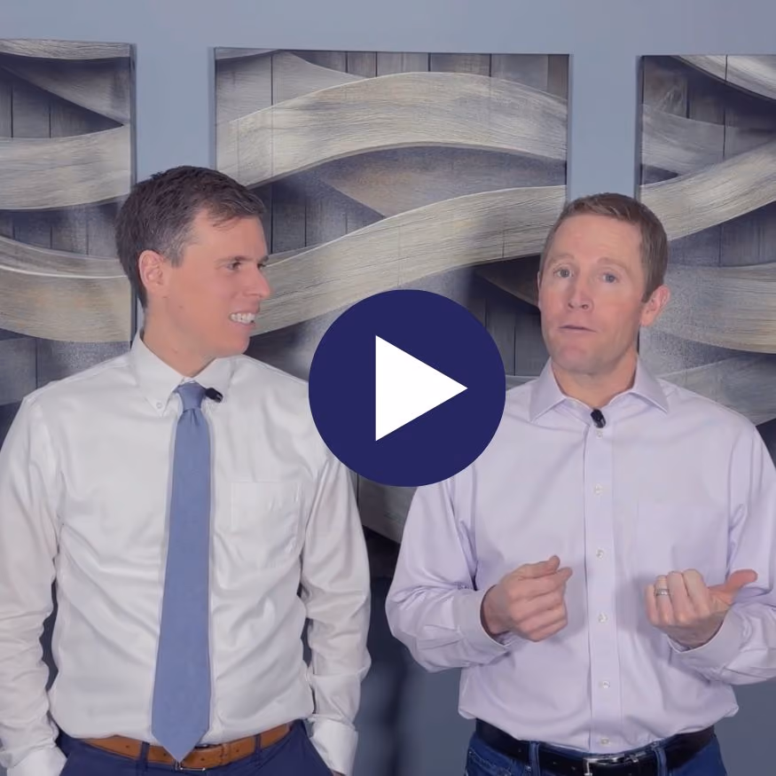 Two men in dress shirts talk in front of abstract wall art, with a play button overlay in center.