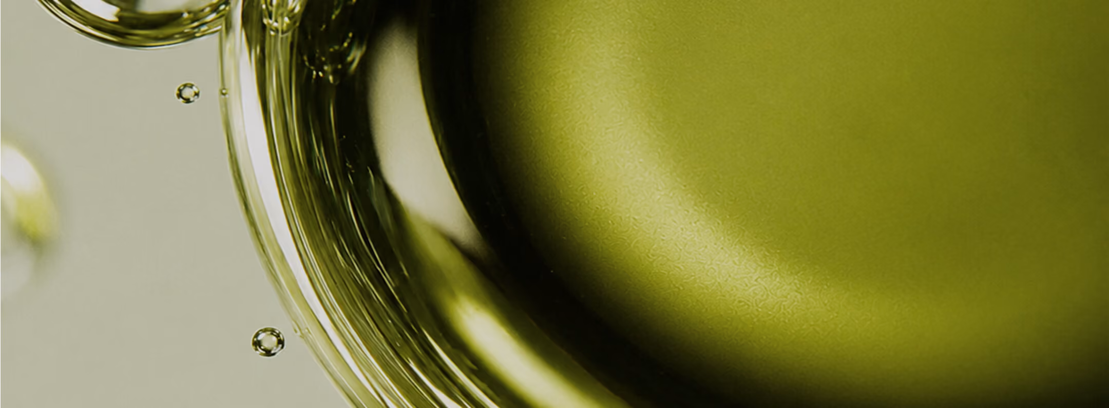 Close-up of translucent bubbles and a smooth surface with greenish-gold hues, showing light reflections and texture.