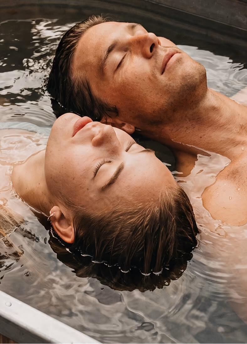 A man and a woman with closed eyes are peacefully floating on their backs in water, their heads close together.