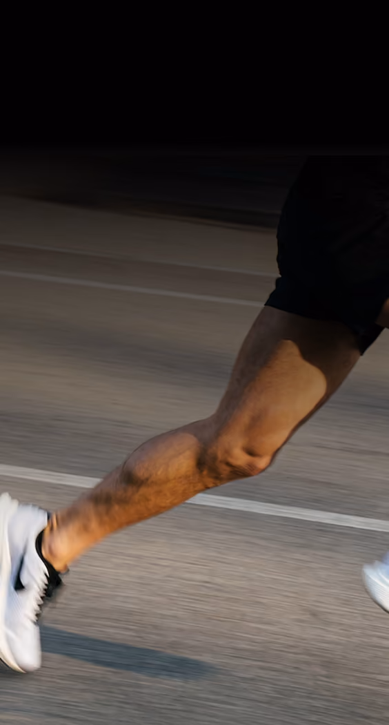 Close-up of a runner's muscular legs in motion wearing white and black athletic shoes on a paved road.