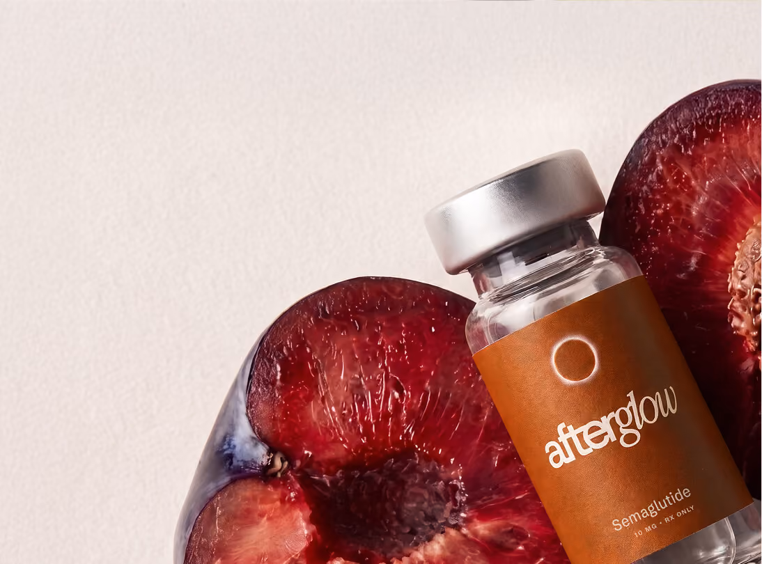 Glass vial labeled 'afterglow Semaglutide 30 MG RX ONLY' resting on two halves of a dark red plum on a light background.
