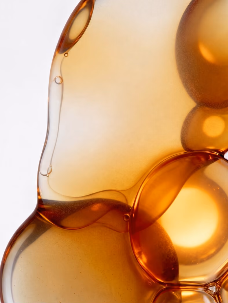 Close-up of translucent amber-colored overlapping oil droplets with smooth edges and light reflections on a light background.
