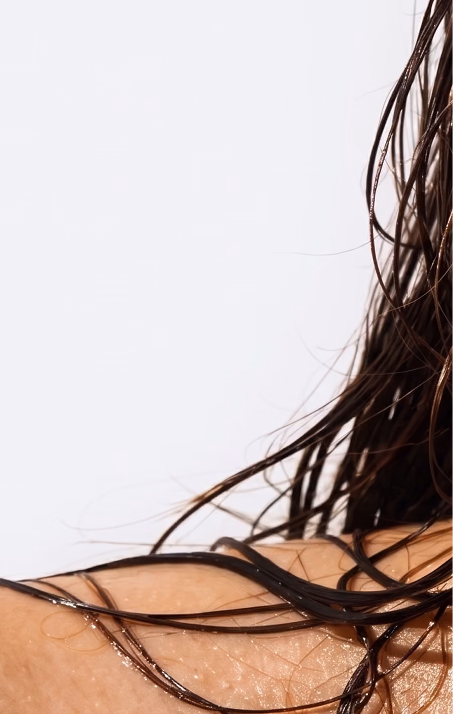 Close-up of a woman's wet neck and shoulder with strands of dark wet hair resting on her skin against a light background.