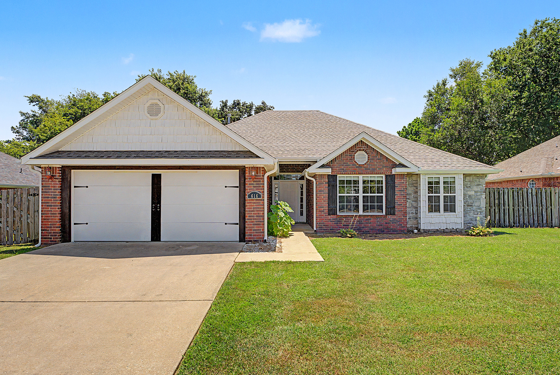 Front entry of a red brick home with two double windows and white garage with decorative handles