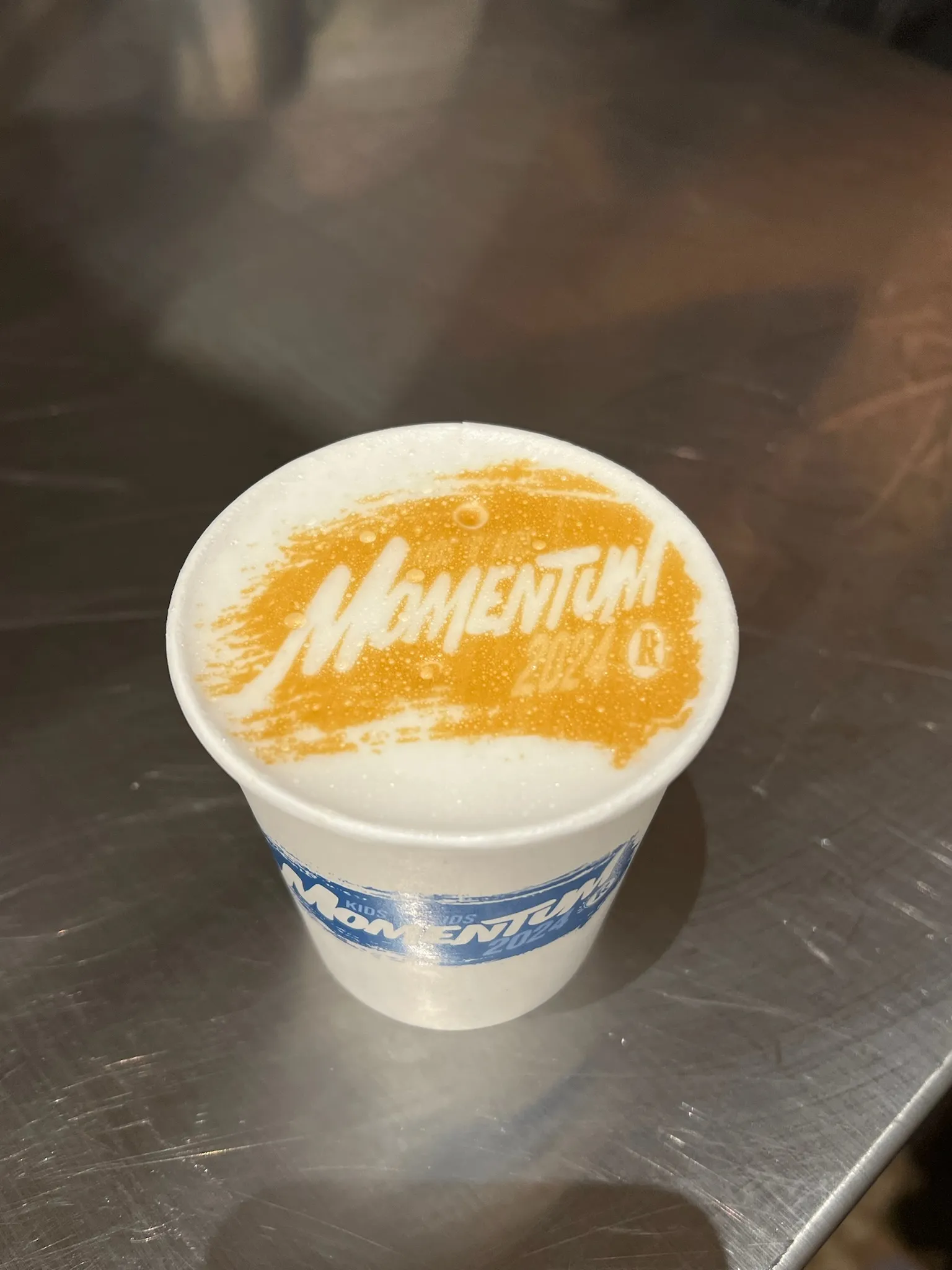 Latte with a Momentum 2024 logo printed in the foam, served in a branded cup