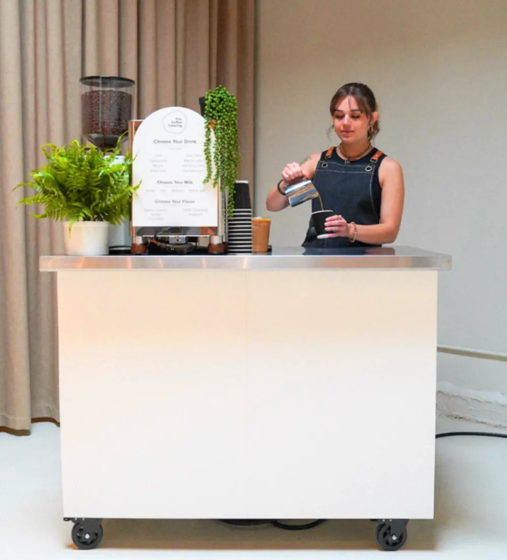 Barista pouring steamed milk at a white Vim coffee cart set up indoors