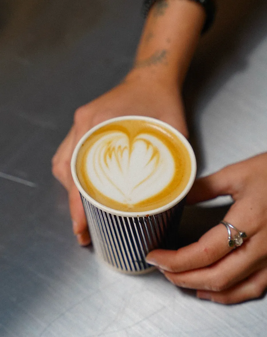 Hands holding a latte with heart-shaped latte art in a ribbed paper cup