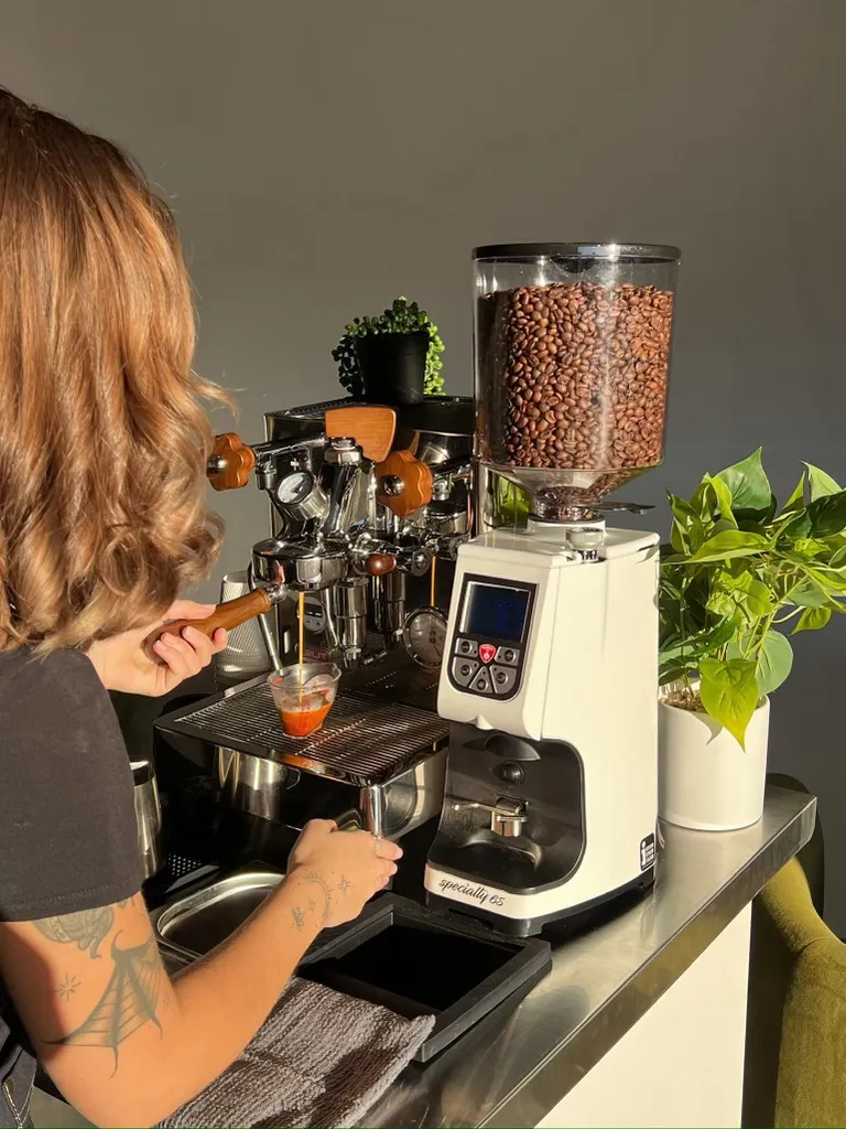 Barista pulling an espresso shot on the cart's machine beside a full coffee grinder