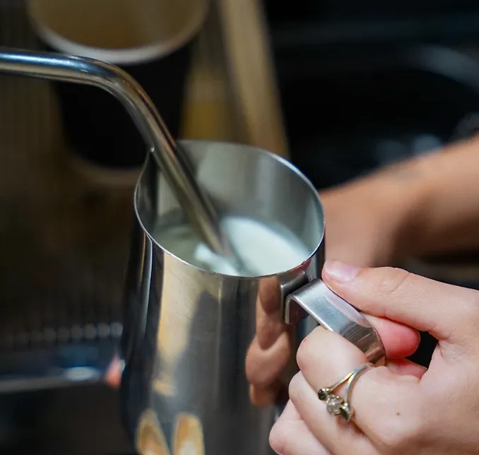 Barista holding a steaming pitcher of freshly steamed milk at an espresso machine
