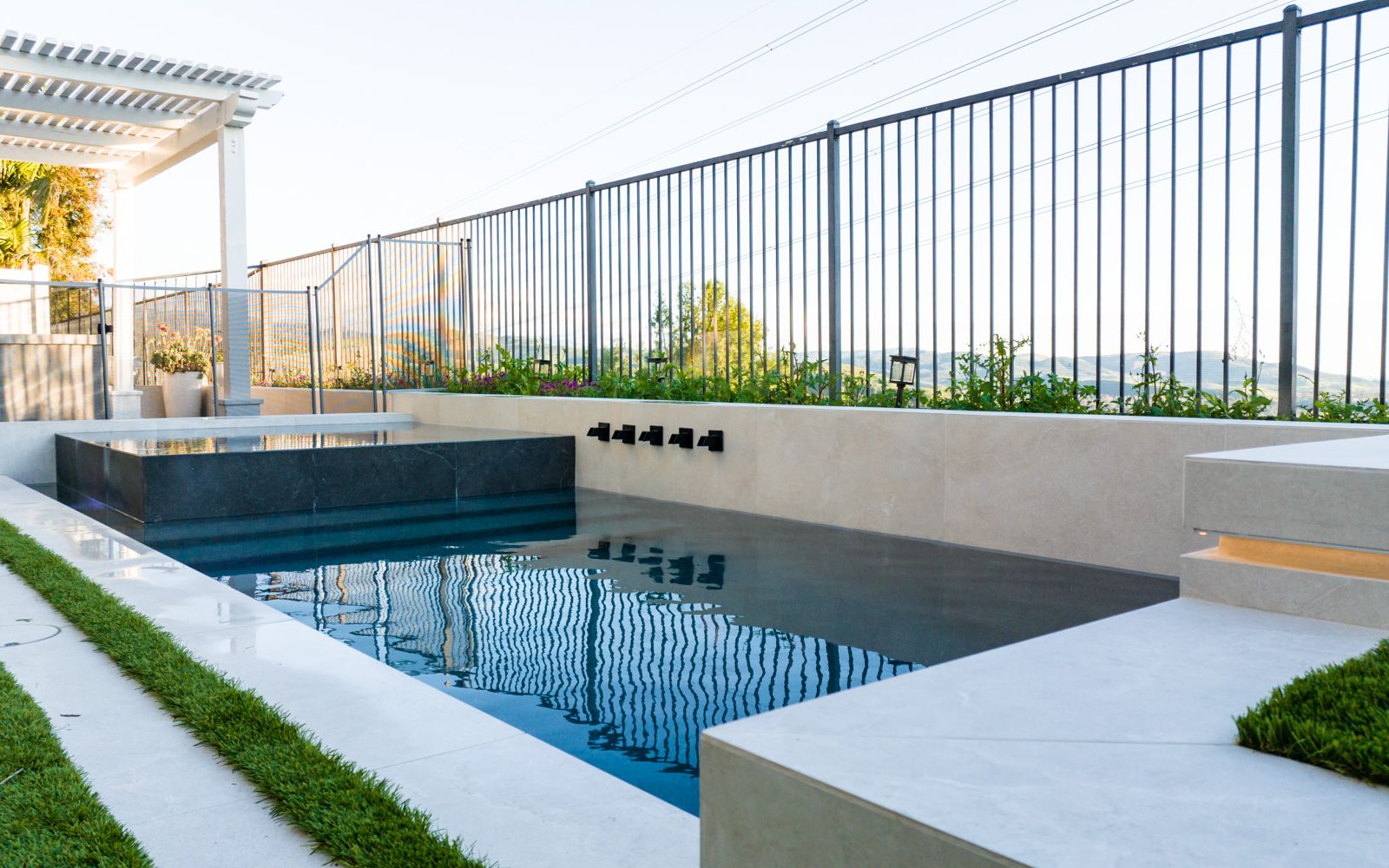 A long rectangular pool with a raised spa, pale coping, narrow turf strips, and an open ridge view.