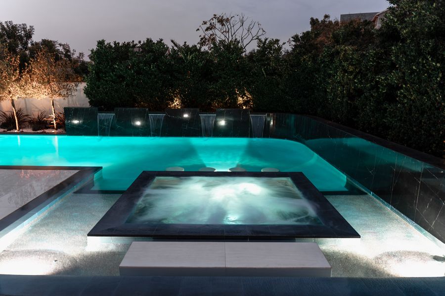 Dark tile raised spa lit from within at night, water almost black at the edges.