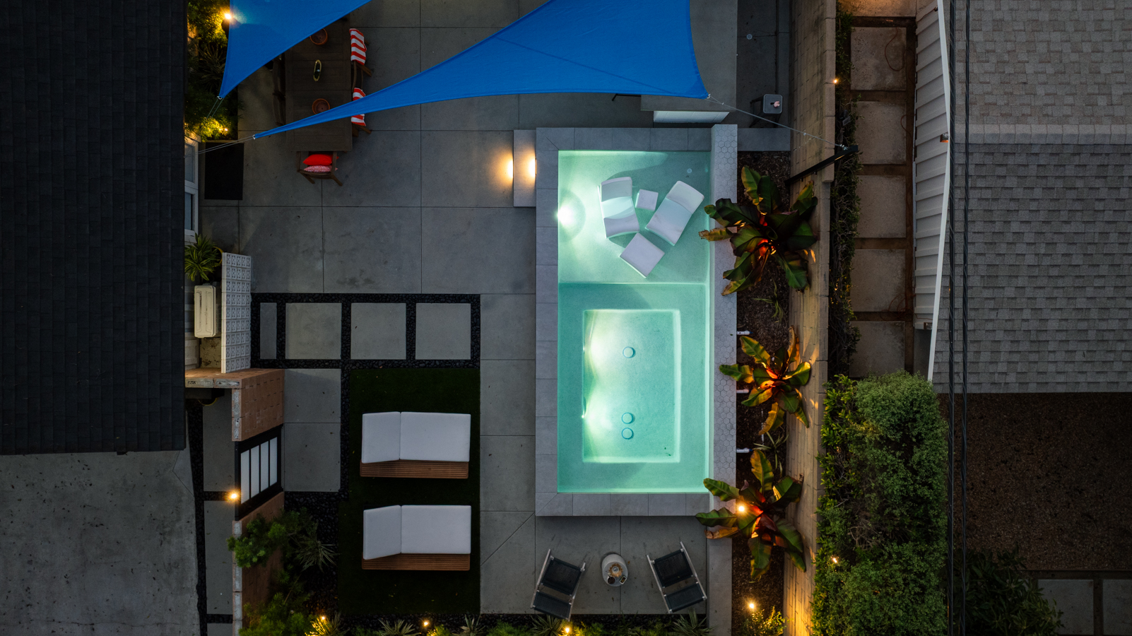 A raised spa glowing at night beside a pool, fireplace, water bowl, and planted wall.