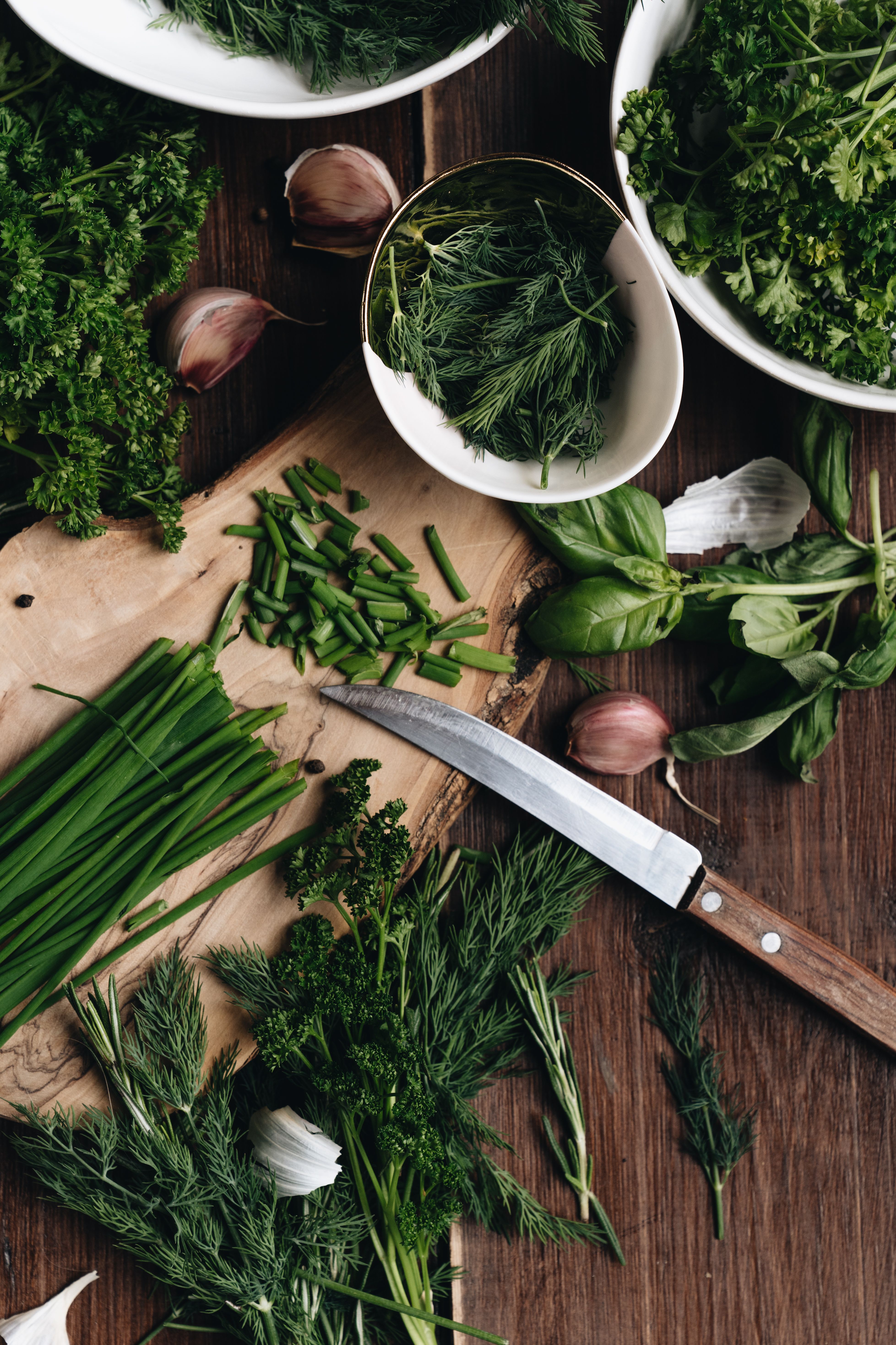 Fresh herbs and garlic on a dark wooden prep table.