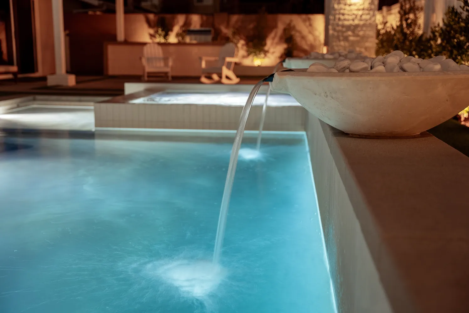 Close on a water bowl spilling into the pool at night, the water lit pale green beneath it.