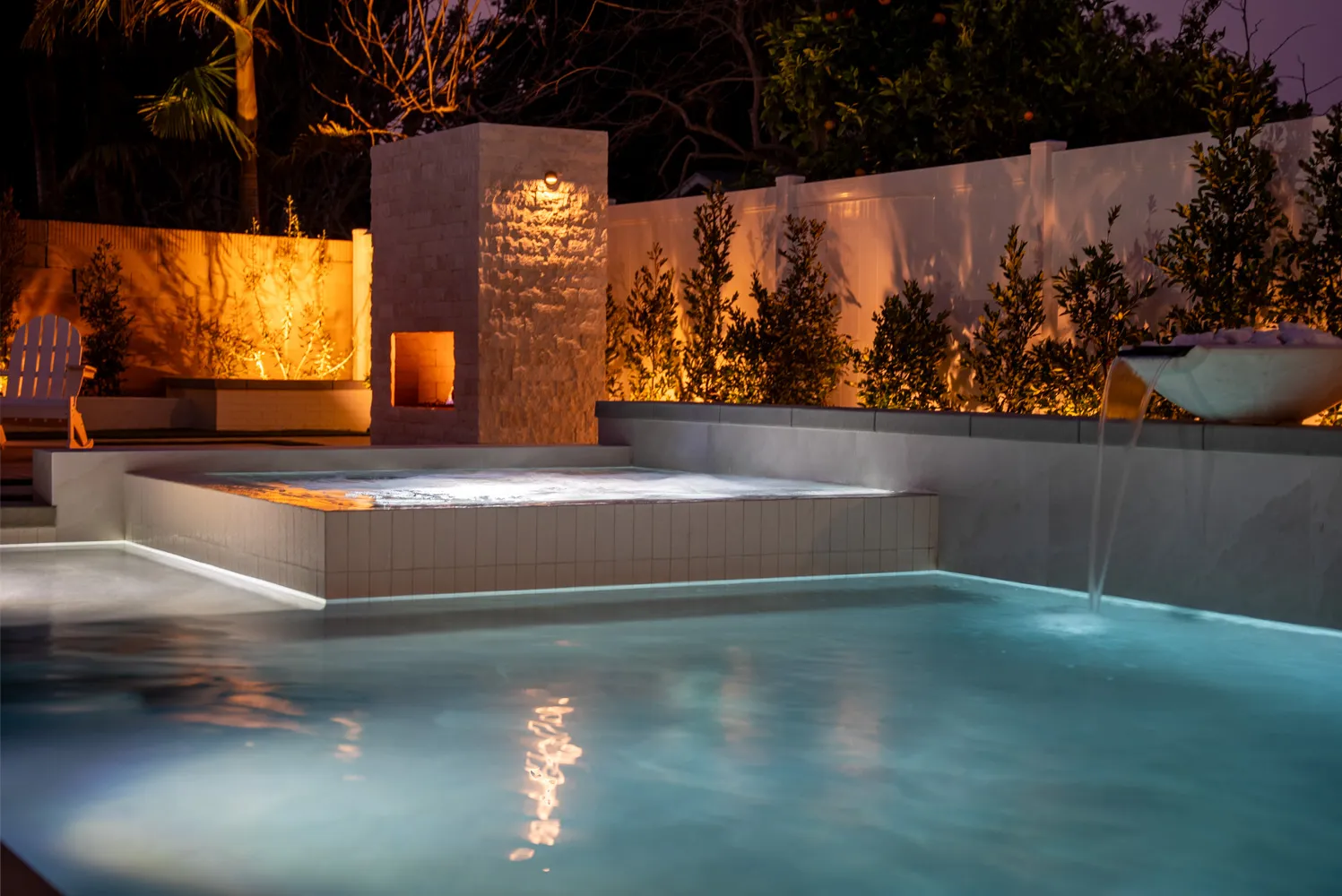 The fireplace tower burning after dark, its light carrying across the spa and the still surface of the pool.