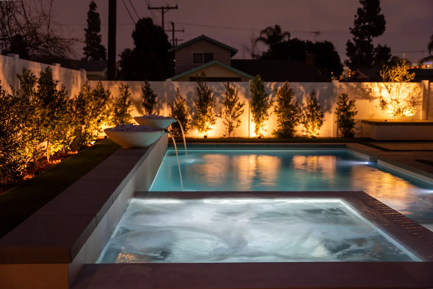The spa foaming after dark beside the lit pool, the planted wall glowing amber behind.