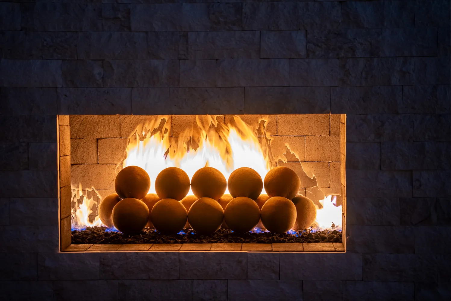 Flame across a row of ceramic spheres inside the stacked-stone firebox.
