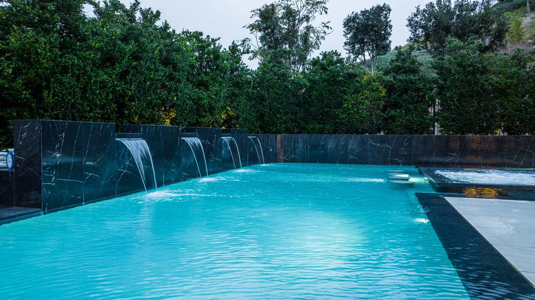 A vanishing edge running the width of the frame, sheet waterfalls falling into the pool and a treeline sitting level with the far lip.