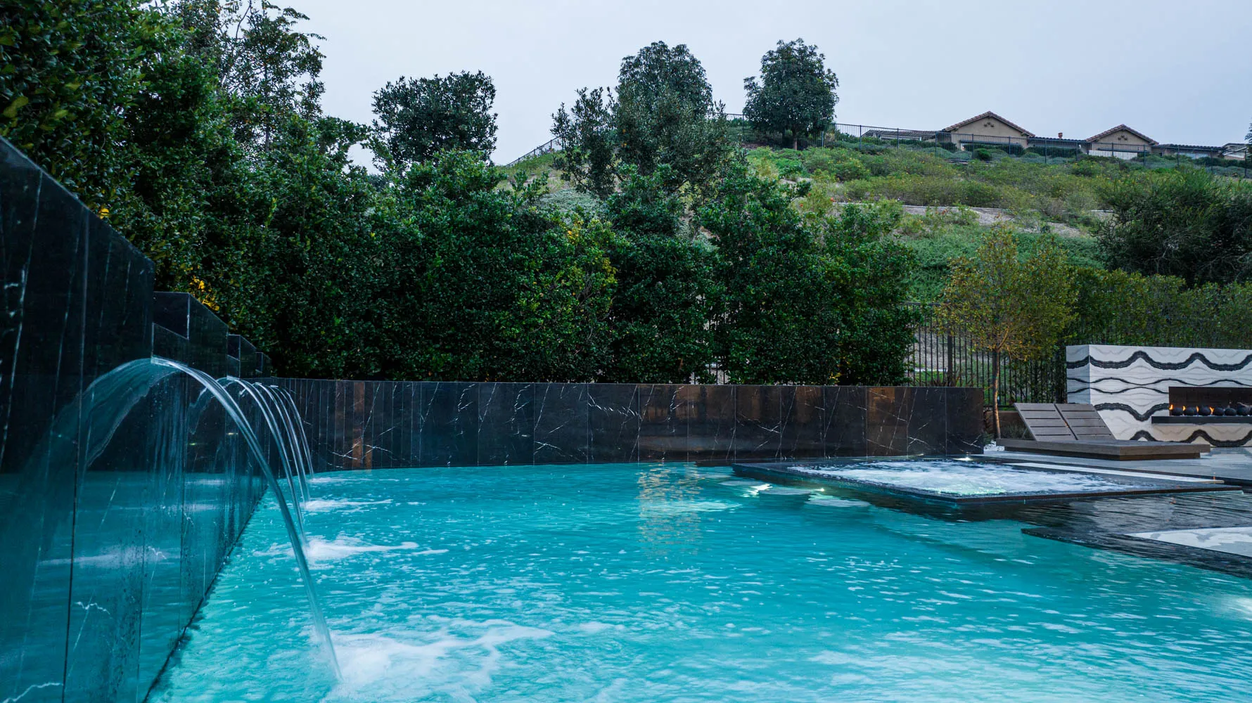 Deck jets arcing into turquoise water, with a dark stone wall along the near edge and hills beyond.