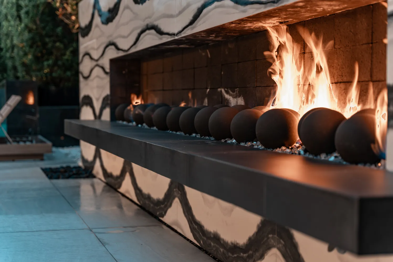 Close on the burner, flame running the length of a row of dark ceramic spheres.