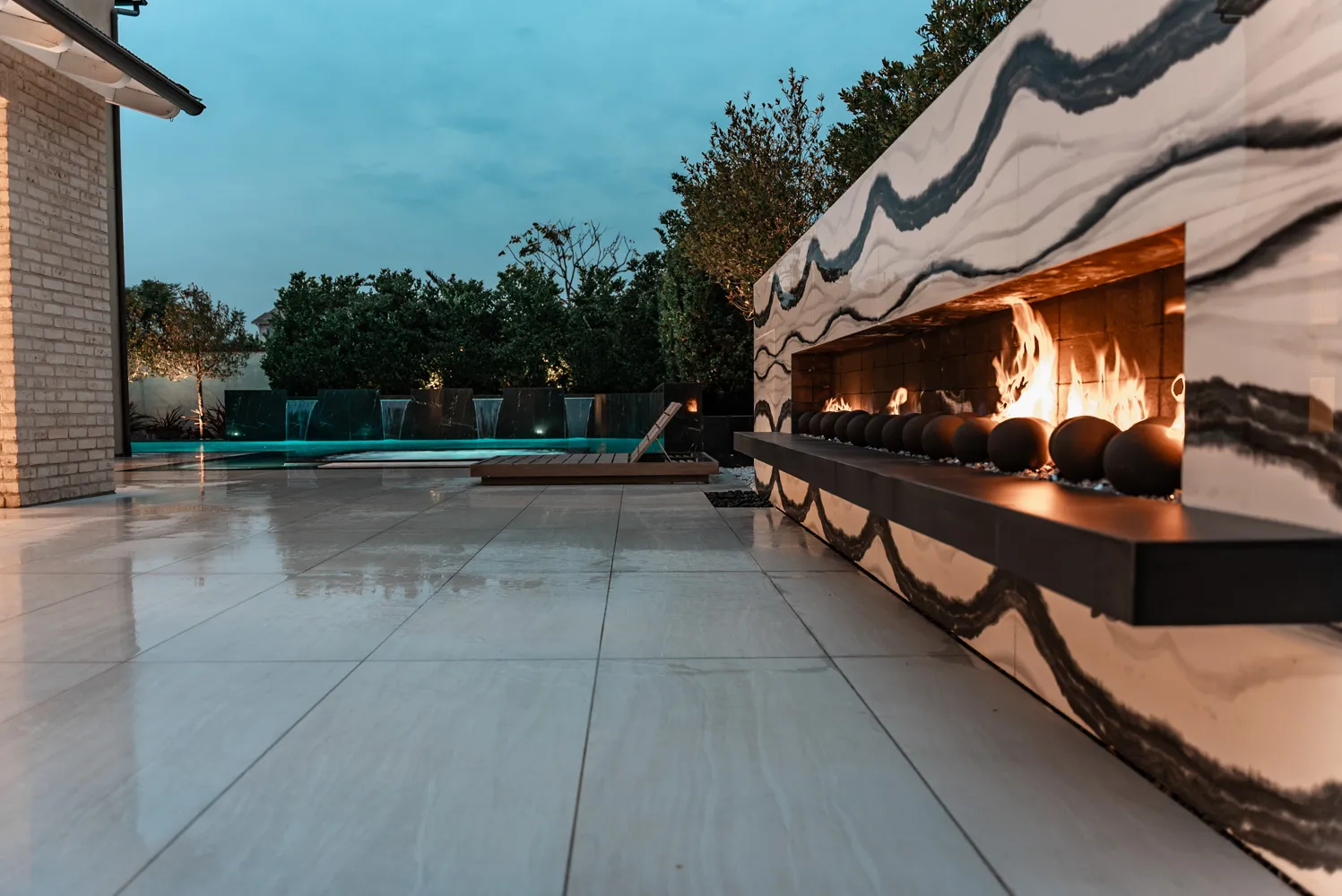 The fireplace wall from an angle at dusk, a row of dark spheres glowing along the burner.