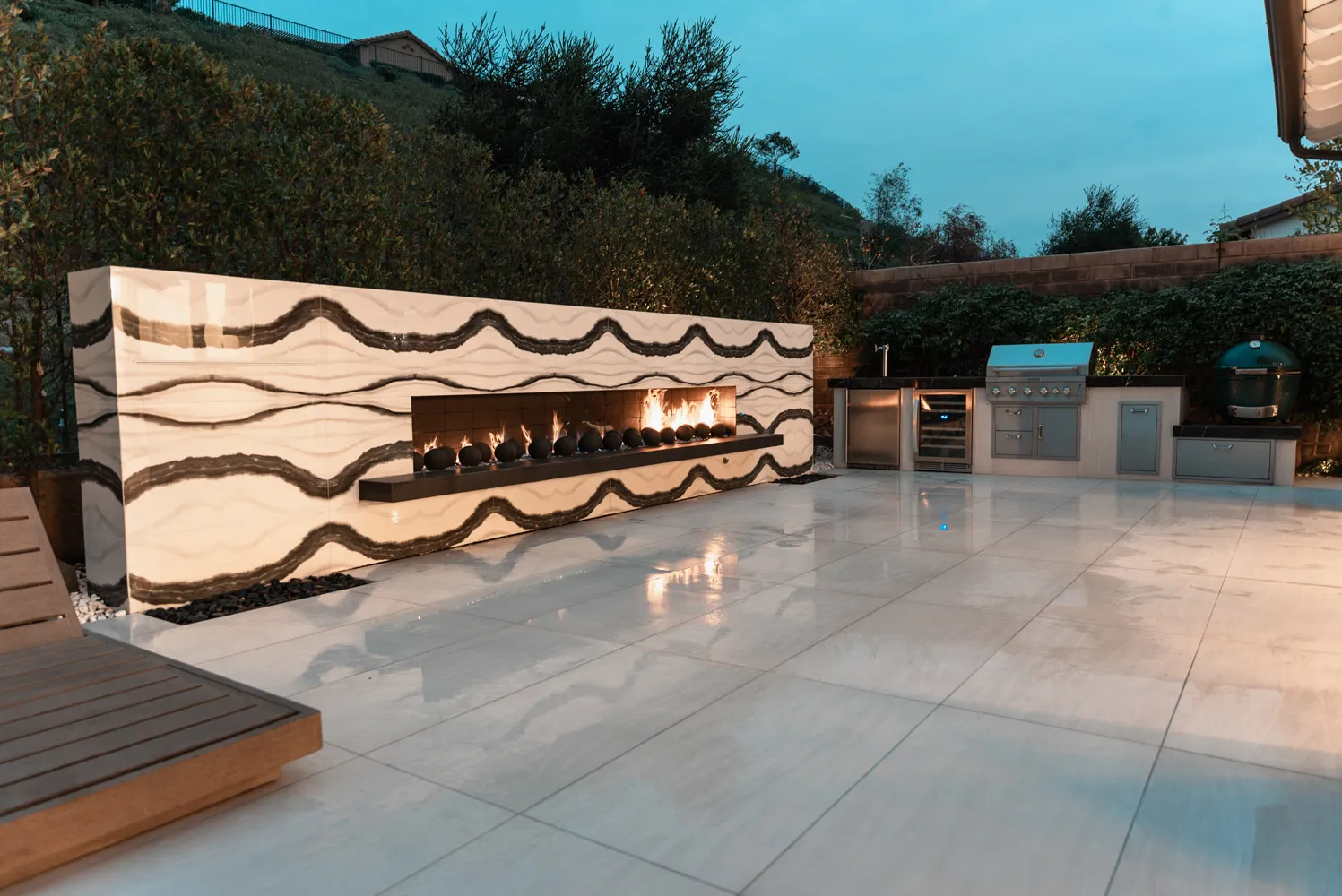 The fireplace wall and outdoor kitchen together at dusk, with the hillside falling away behind.