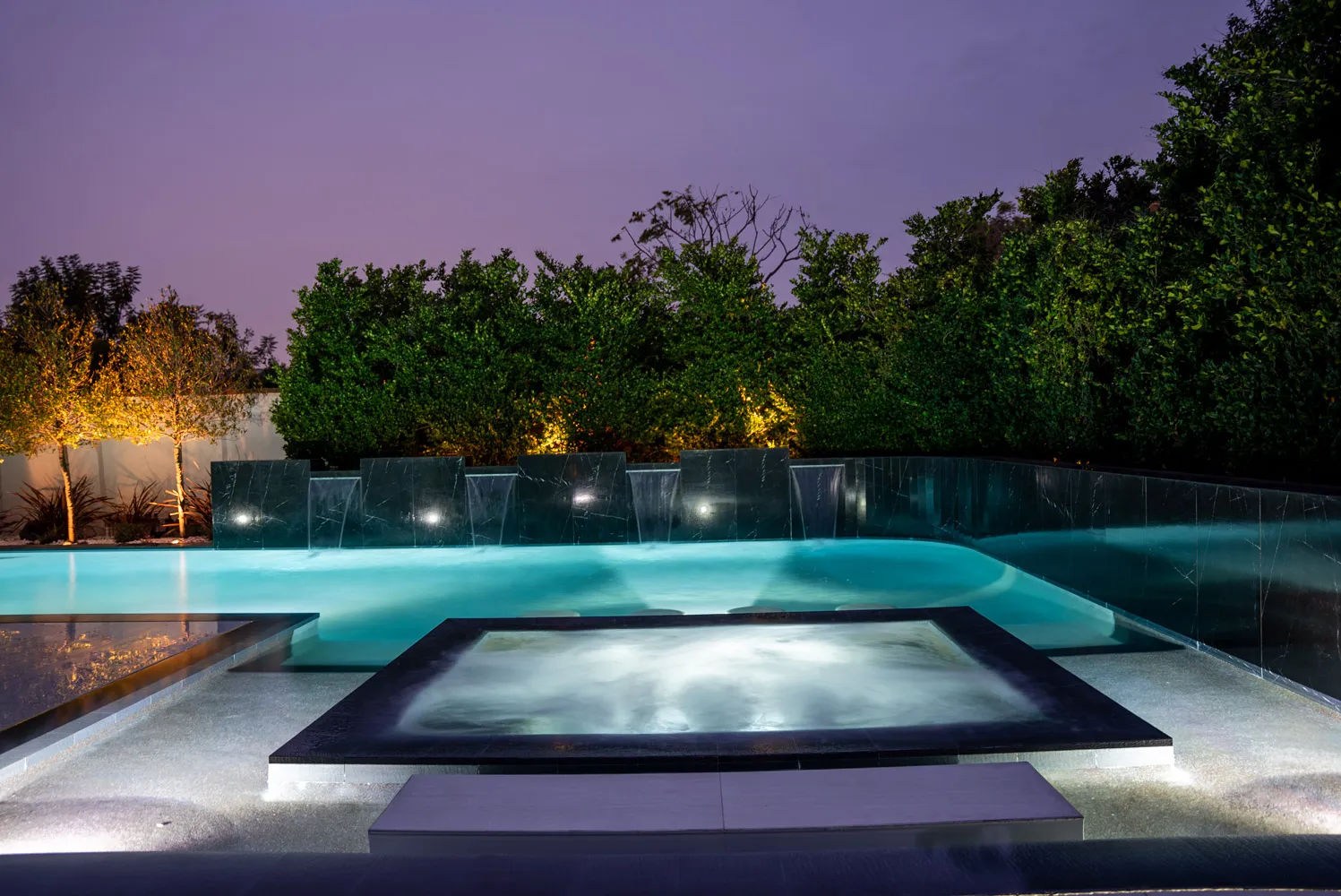 The spa and pool under a violet sky, the hedge behind lit low and warm.