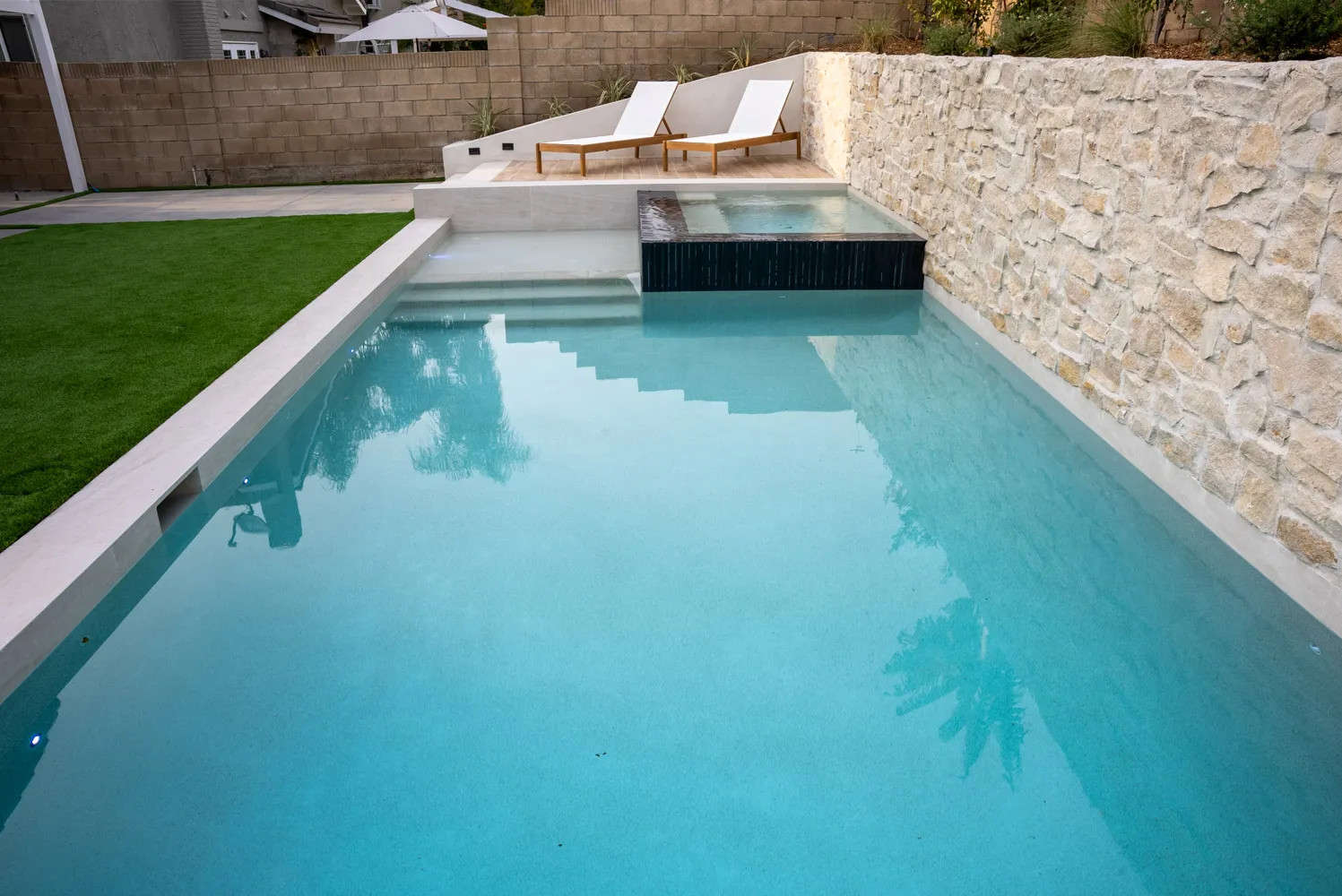 The pool from the deep end, entry steps at the near corner and a raised spa beyond.