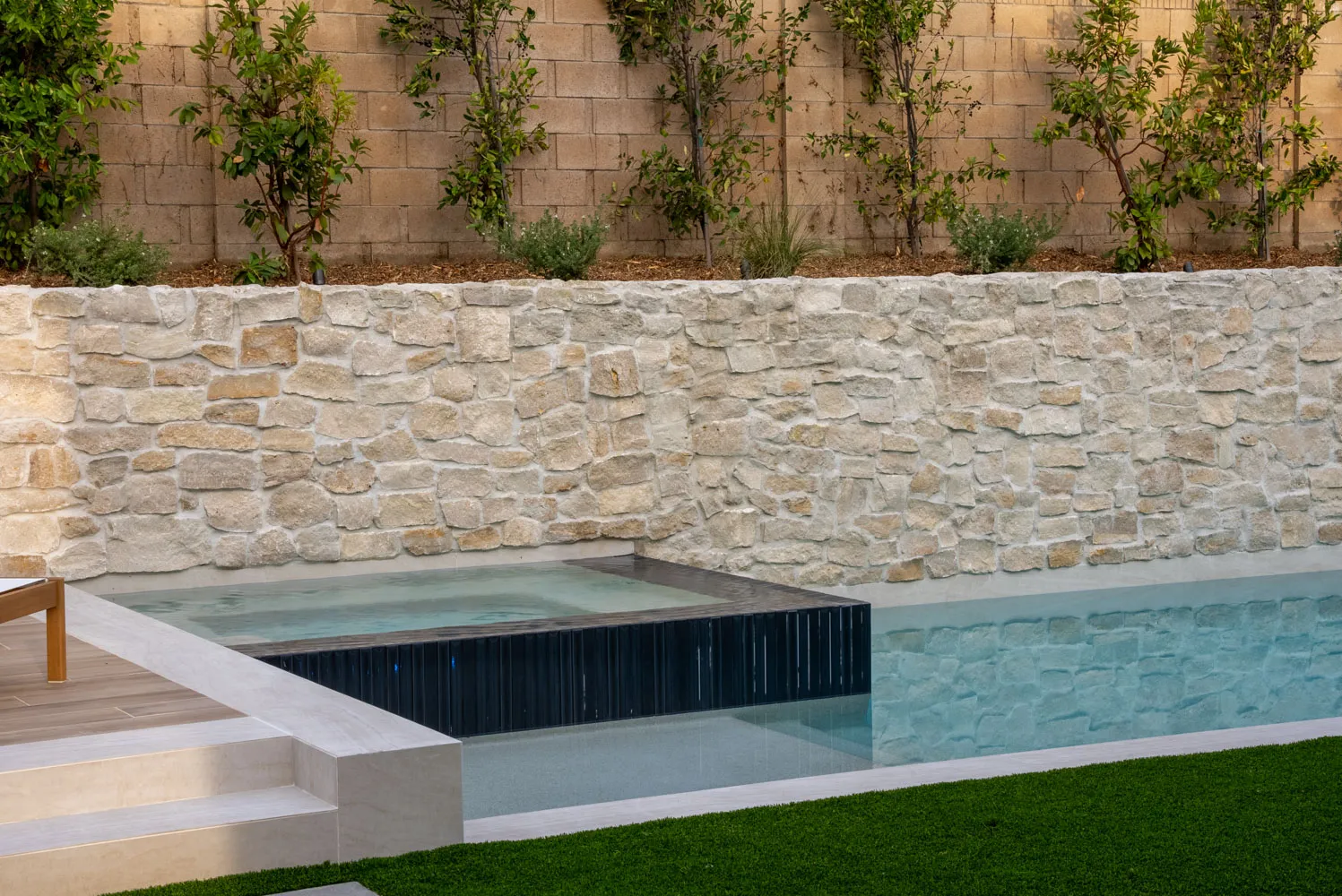 The spa set into the end of the pool in evening light, stone wall above and turf running along the side.
