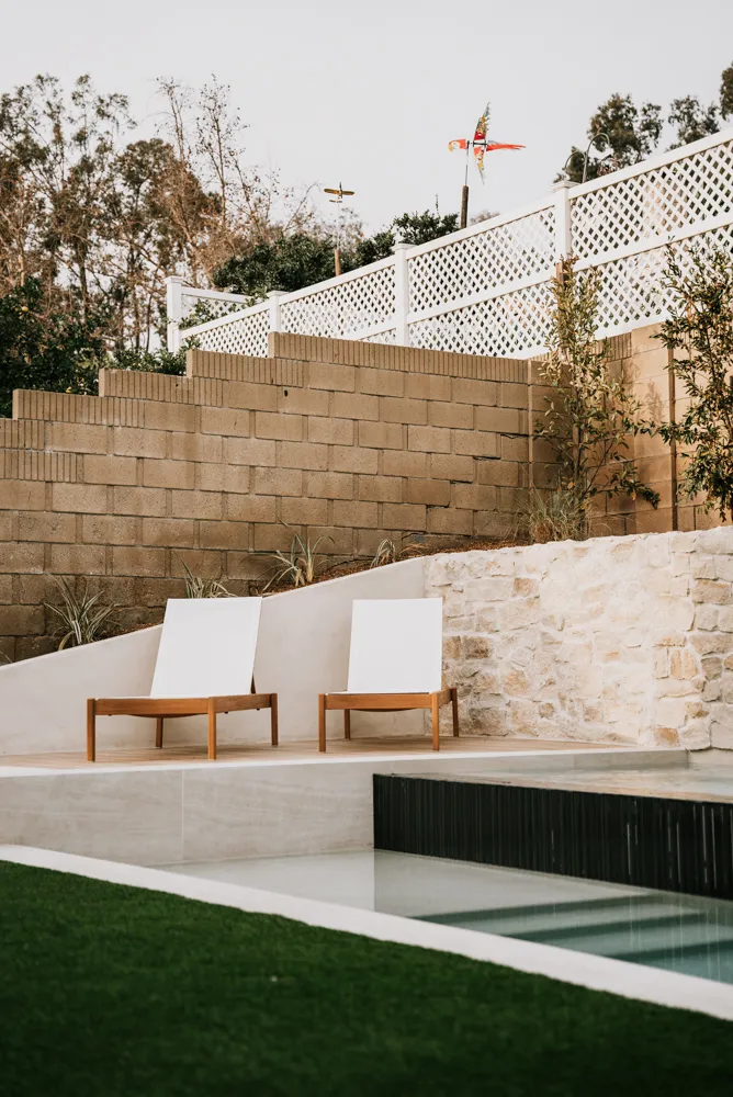 Loungers on the upper terrace with the spa below them, a block retaining wall and lattice fence stepping up the slope behind.