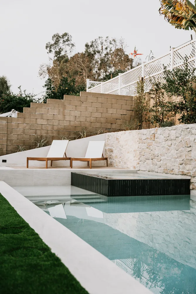 The pool running away below the loungers, the stacked-stone wall along its far side.