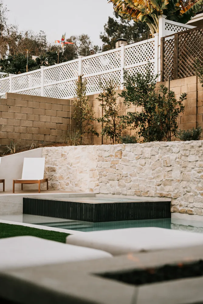 A fire feature in the near foreground with the spa and stone wall held soft behind it.