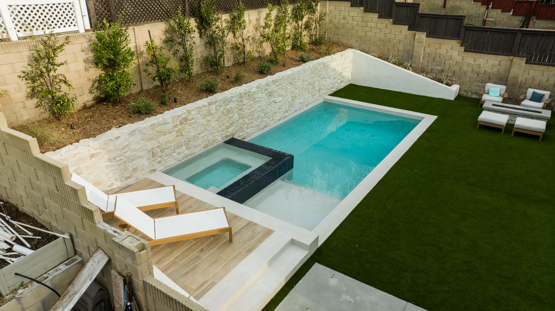 The yard from above, the pool and spa running along the stone wall with turf on either side.