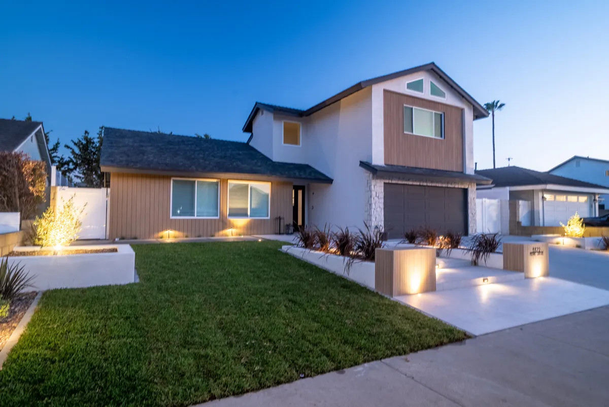 The front of the house at dusk, lawn and pathway lit low, planting in rendered planters along the drive.
