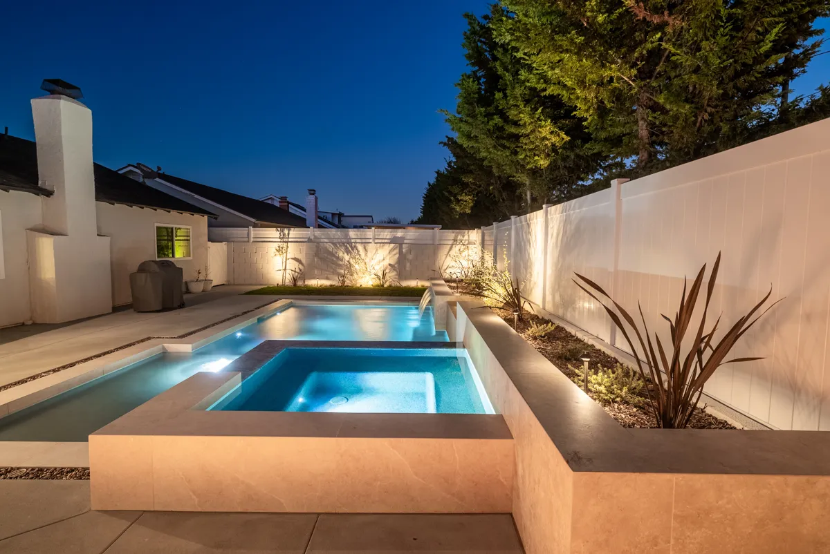 A raised spa with a stone-clad face standing at the end of the pool, spiky planting lit beside it.