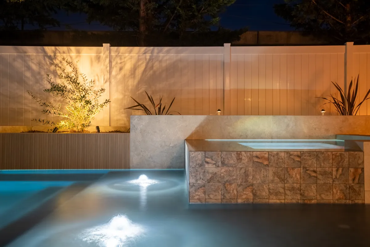 The spa spilling into the pool after dark, its stone-faced wall catching the light from the water.