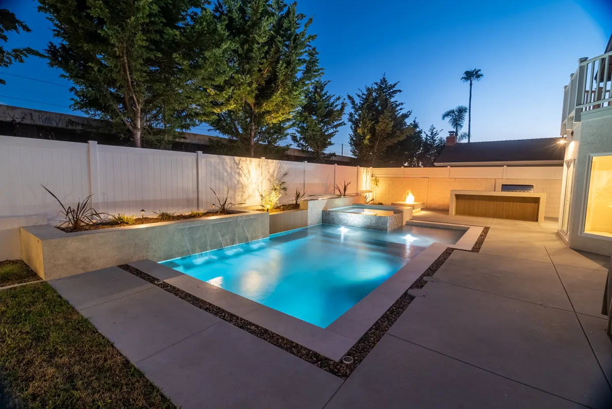 The pool from its far corner, spa beside it and the wall and trees washed warm from below.