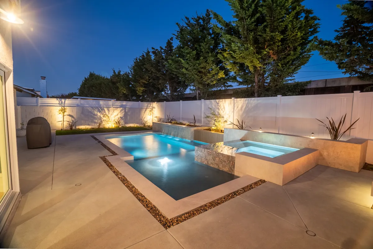 The pool and raised spa at blue hour, planting uplit along the boundary wall.