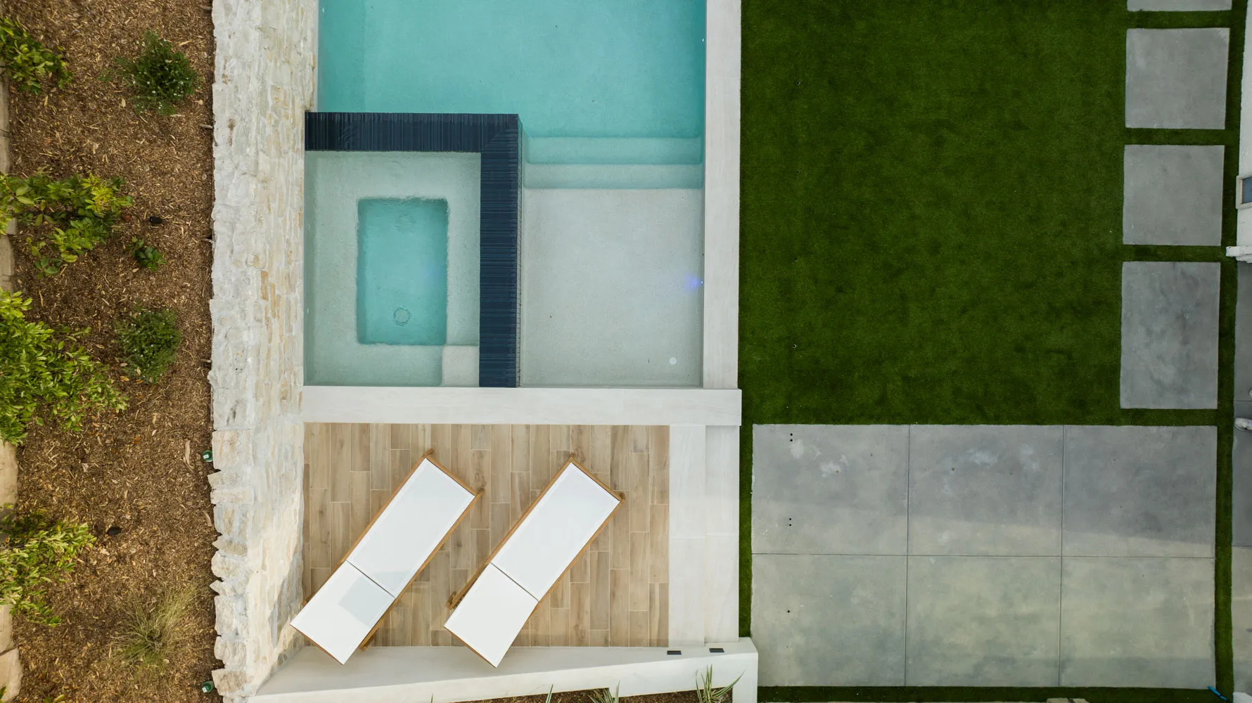 Straight down onto the spa and two loungers, turf squared off around the paving.
