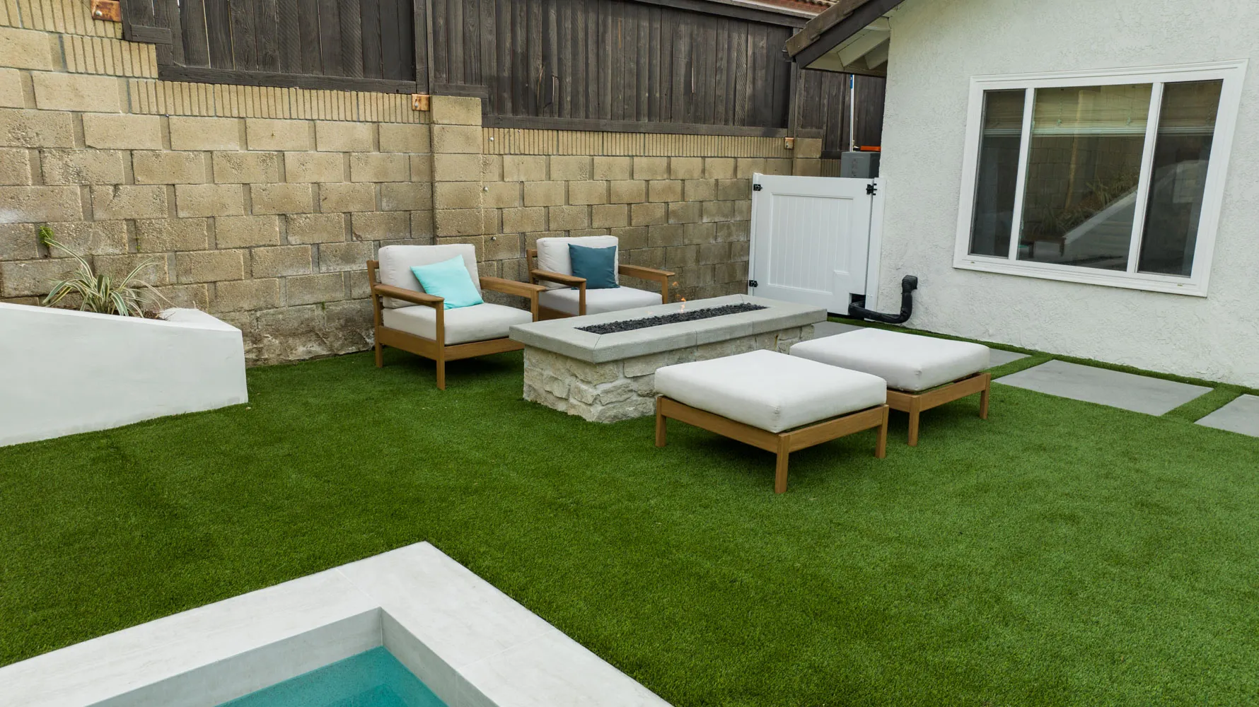 A seating group around a fire table on the turf beside the pool, the house wall behind.