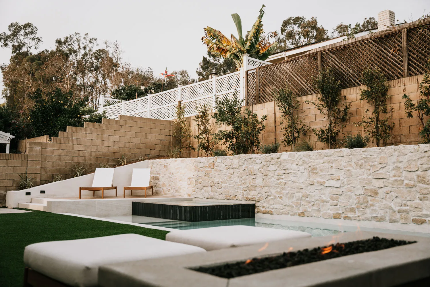A low fire table burning beside the pool, the spa and retaining wall standing behind.