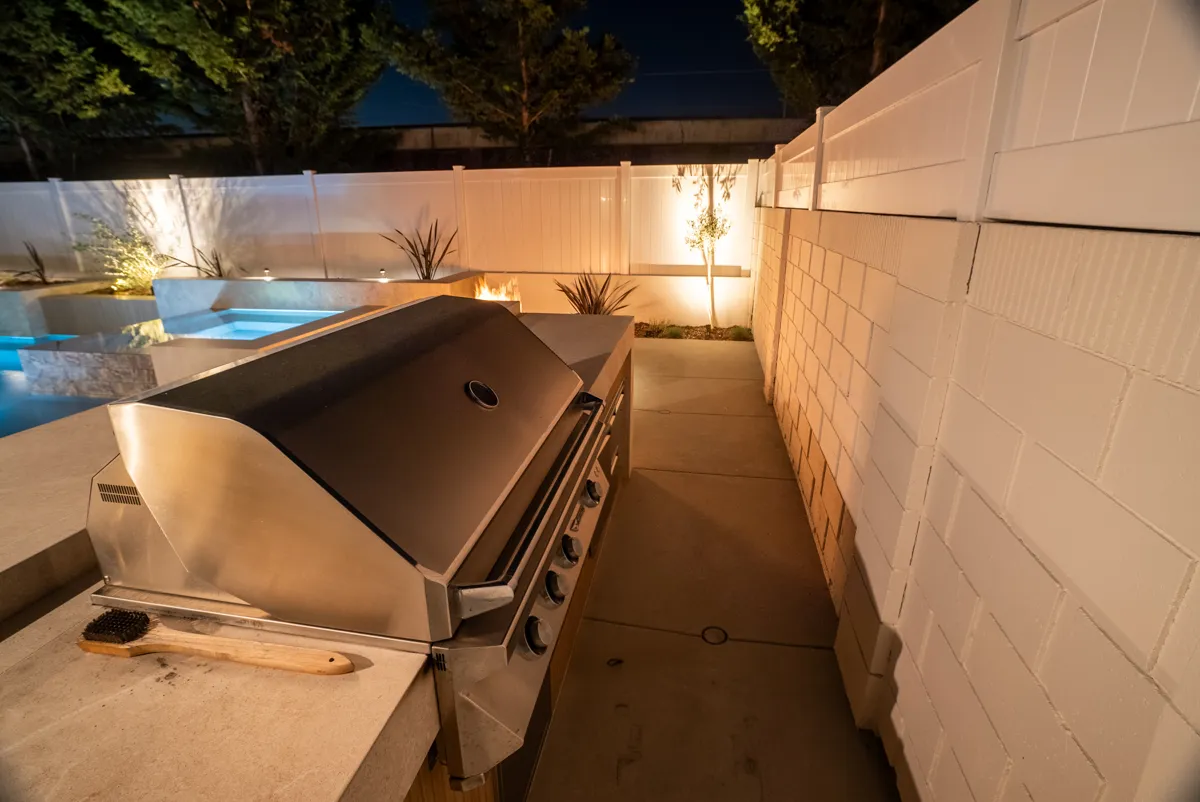 The built-in grill on the side deck at night, lid raised, the boundary wall lit behind.