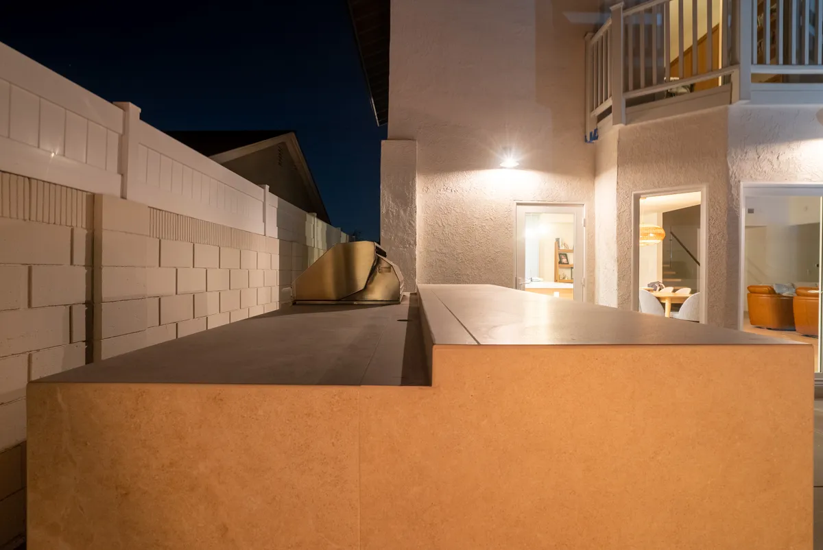 The kitchen counter after dark with the lit interior of the house showing through the doorway.